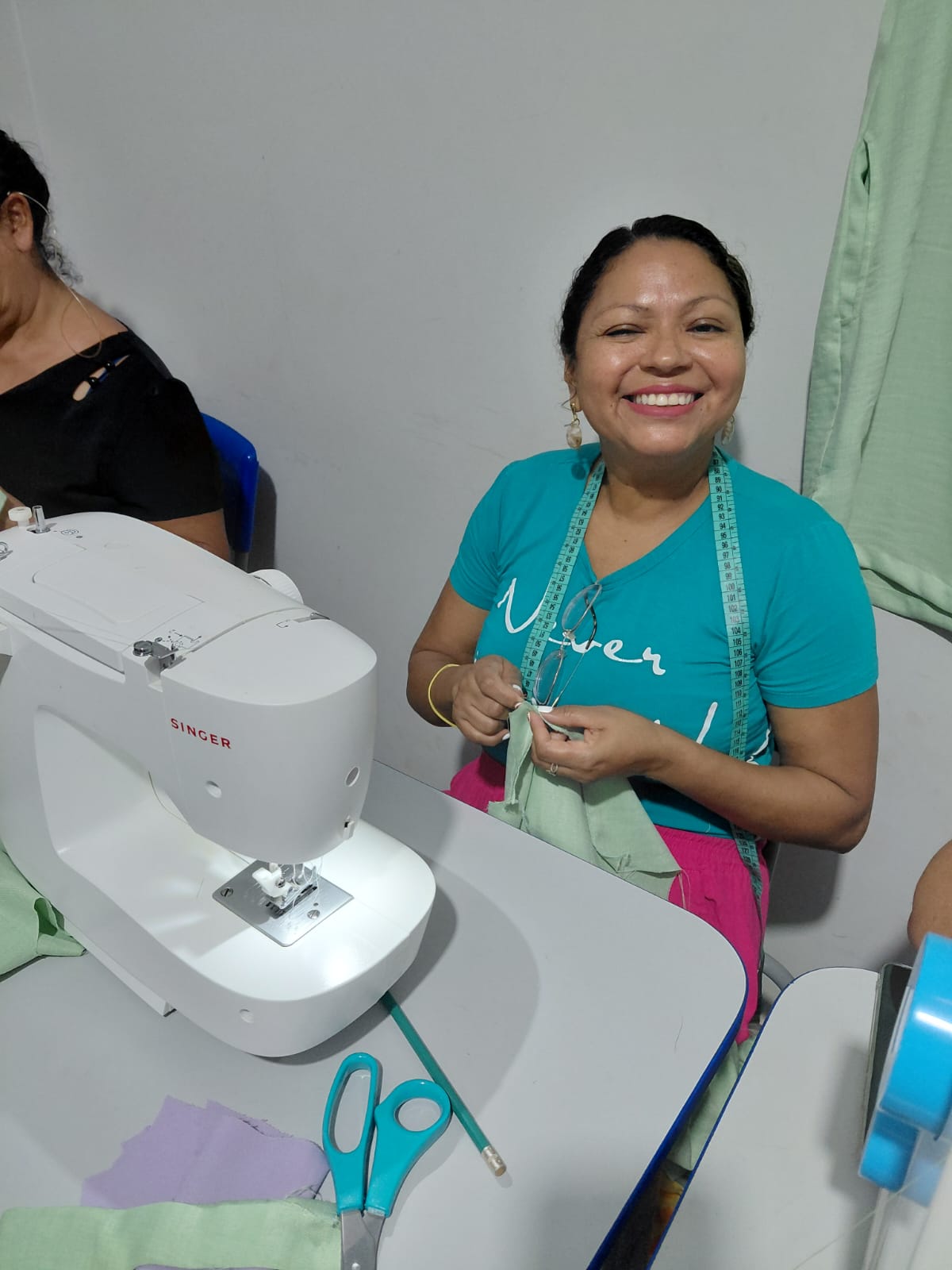 Aluna do curso de corte e costura com fita métrica, cortando tecido na aula