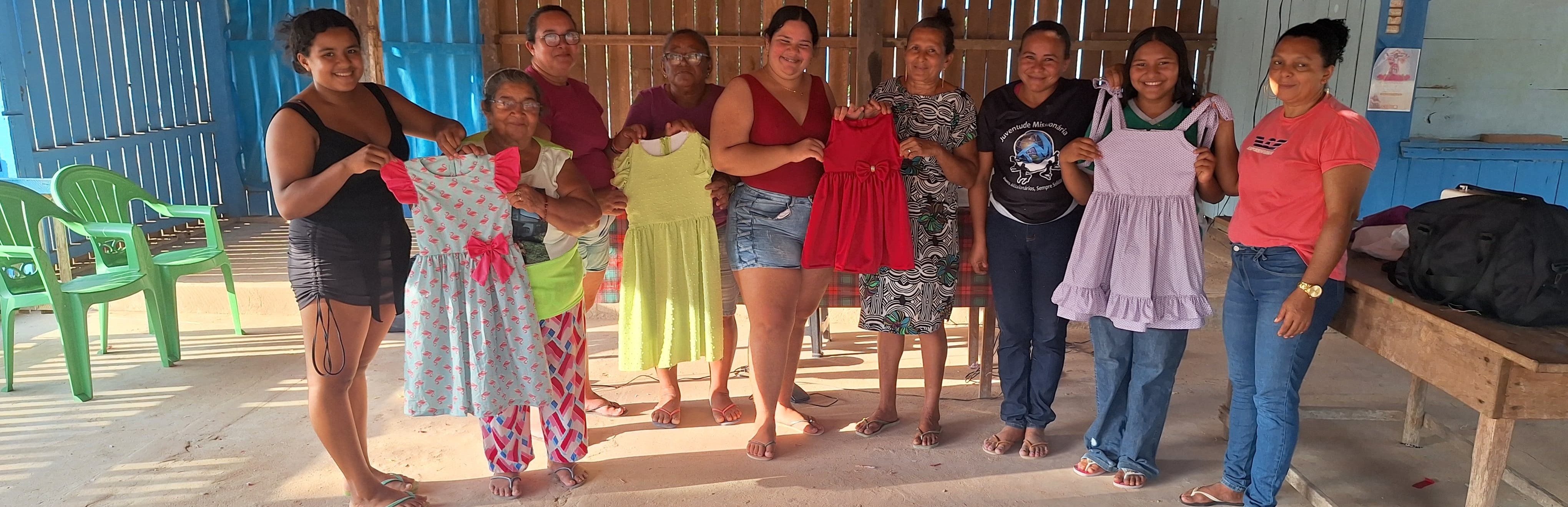 Turma do curso de corte e costura segurando os vestidos que fizeram